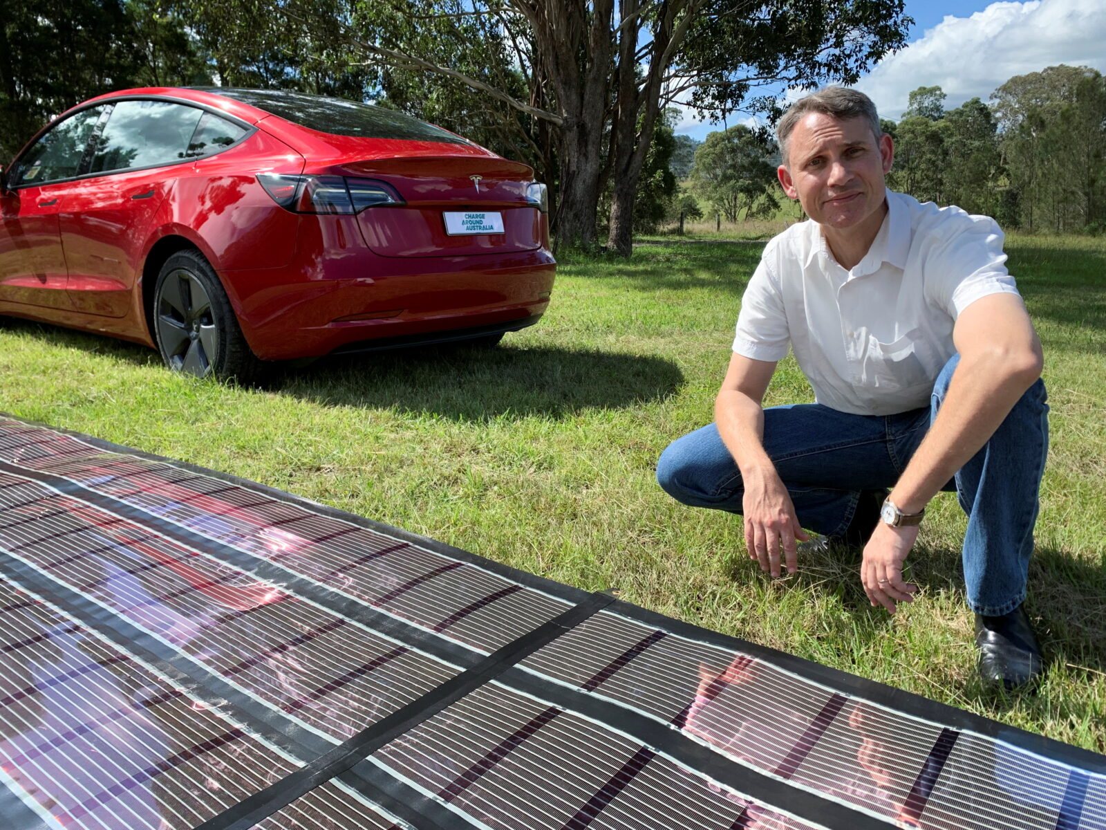 Charge Around Australia project lead and inventor of 'printed solar' panels Paul Dastoor next to a printed solar panel and a Tesla car, in Gosforth