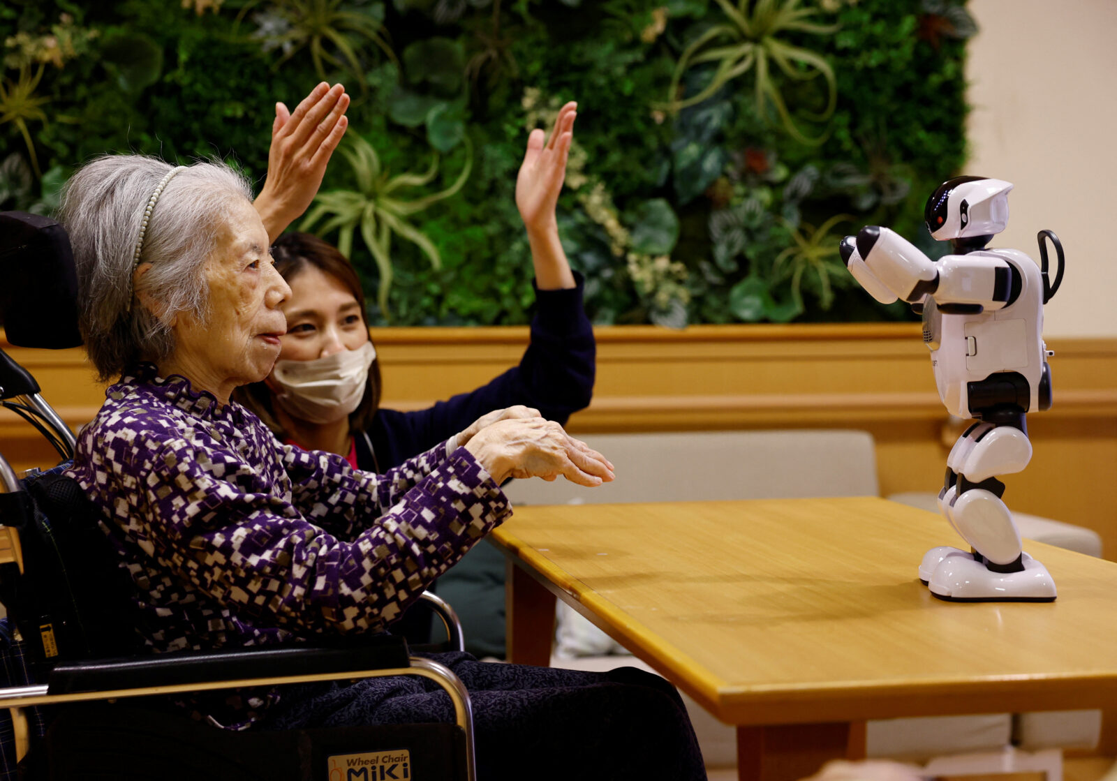 Yukiko Namekata, a resident at an elderly care facility run by Zenkoukai, and her caretaker follow the movement of a miniature humanoid robot PALRO at the facility in Tokyo